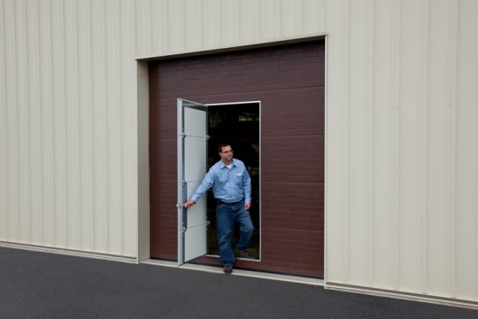 Man exiting door at warehouse through a pass door in a garage door.